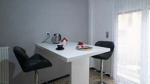Eine kleine Küchenzeile mit weißer Arbeitsplatte, zwei schwarzen Barhocker, einer Kaffeemaschine, einer roten Tasse und einem Teller mit Essen.