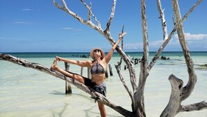 Una persona realizando una postura de yoga sobre una rama, con agua turquesa cristalina debajo.