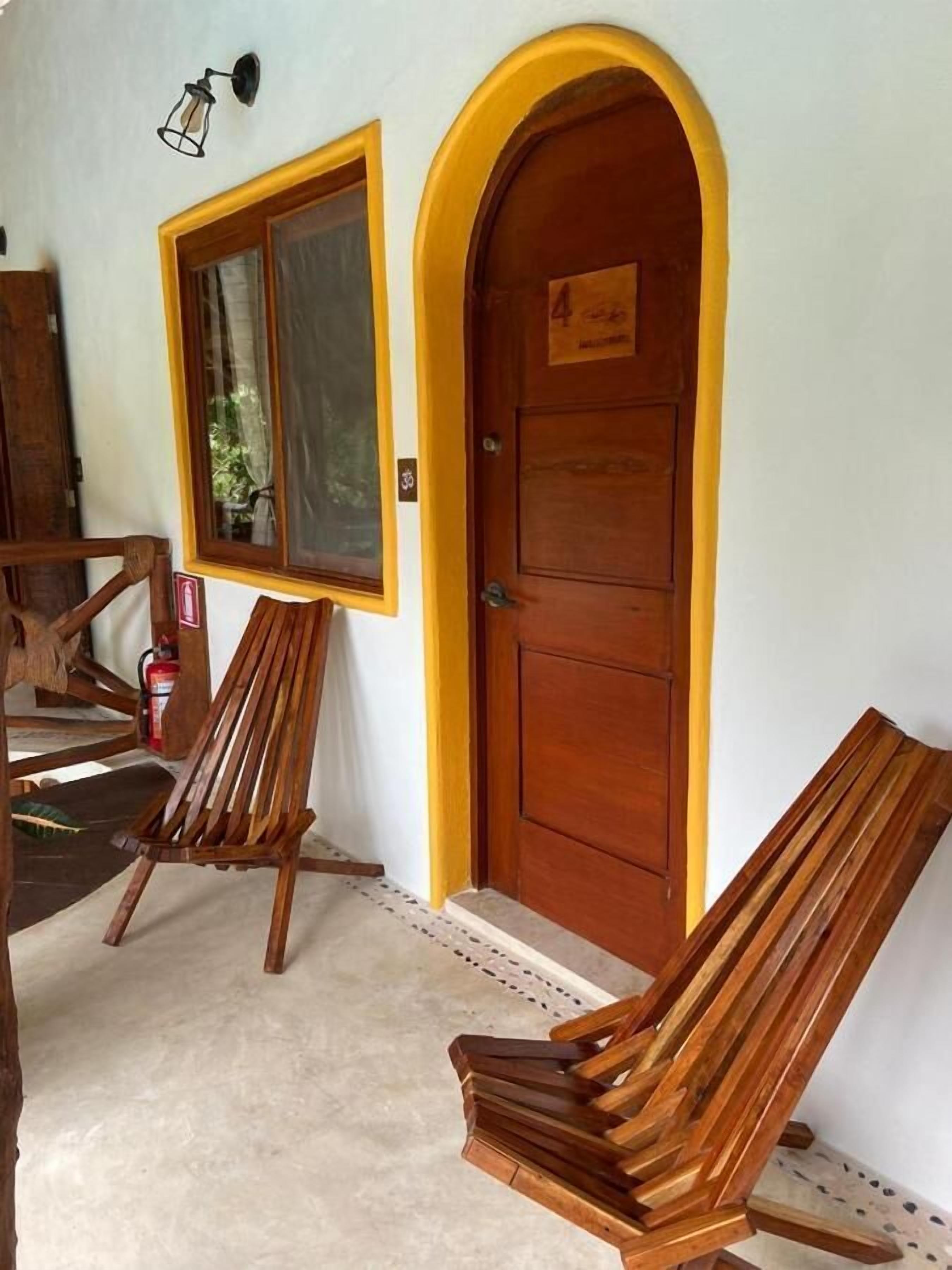 A wooden door with a yellow frame, a window with a curtain, and two wooden chairs.