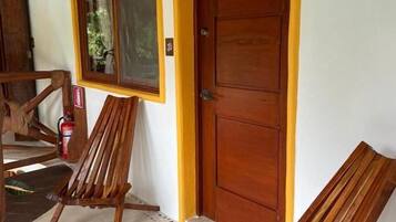 A wooden door with a yellow frame, a window with a curtain, and two wooden chairs.