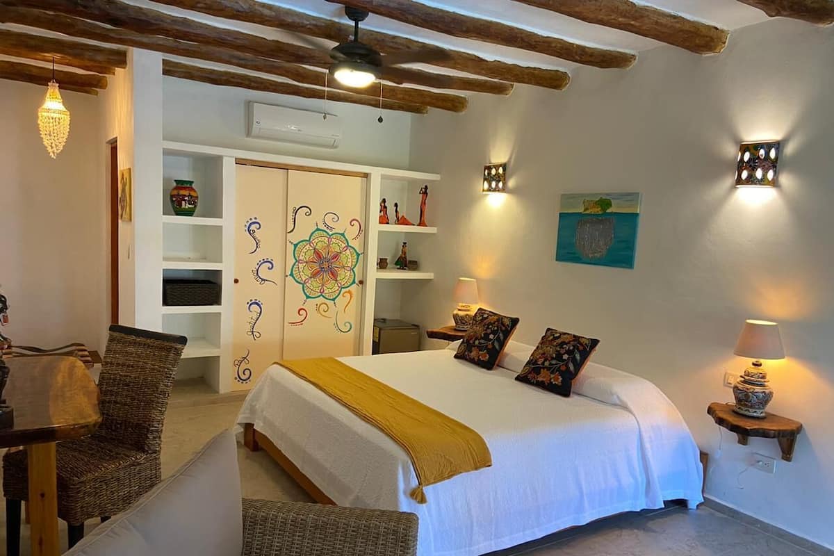 Ein Schlafzimmer mit einem großen Bett, einem Essbereich mit Korbmöbeln und einer Wand mit Kunstwerken.