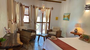 Una habitación acogedora con una cama, dos sillas de mimbre, una mesita y una araña.