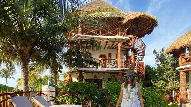 Un resort con terraza de madera, sillas de descanso, piscina y un edificio con techo de paja.