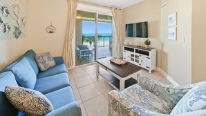 Sala de estar con sofá, mesa de centro y televisor. Balcón con vista al océano.