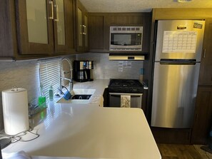 A kitchen with wooden cabinets, a stainless steel refrigerator, a microwave, a stove, and a coffee maker.