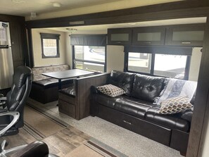 A compact RV interior with a dining area, a sofa, and a kitchenette.