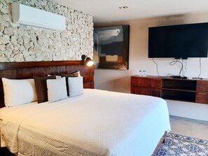 A hotel room with a stone wall, a bed with white bedding, a mounted TV, and a wooden nightstand. - Casa Boutique Pasha (Mérida)