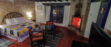 Un dormitorio con cama, una mesa, una silla, chimenea y televisión.