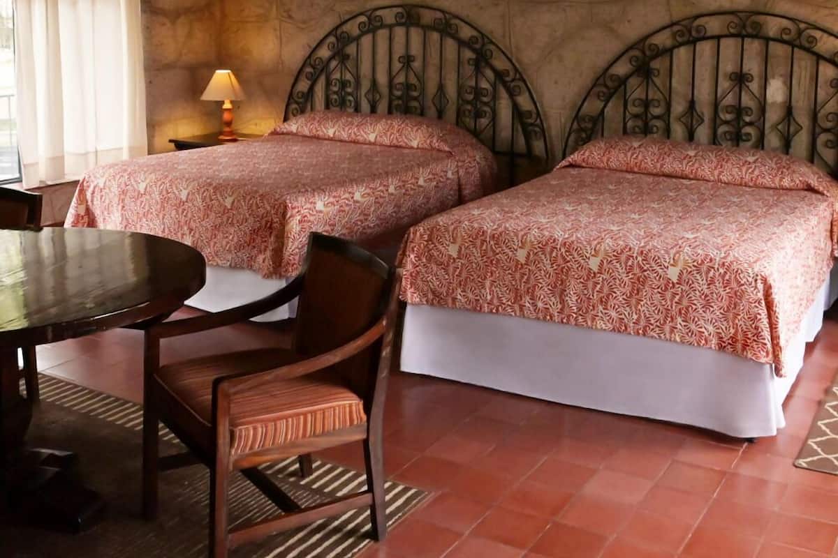 Ein Zimmer mit zwei Betten, einem Tisch und Stühlen. An den Wänden hängen zwei Bilder.