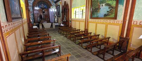 L’intérieur d’une église, avec des bancs en bois, un autel central et des peintures religieuses sur les murs.