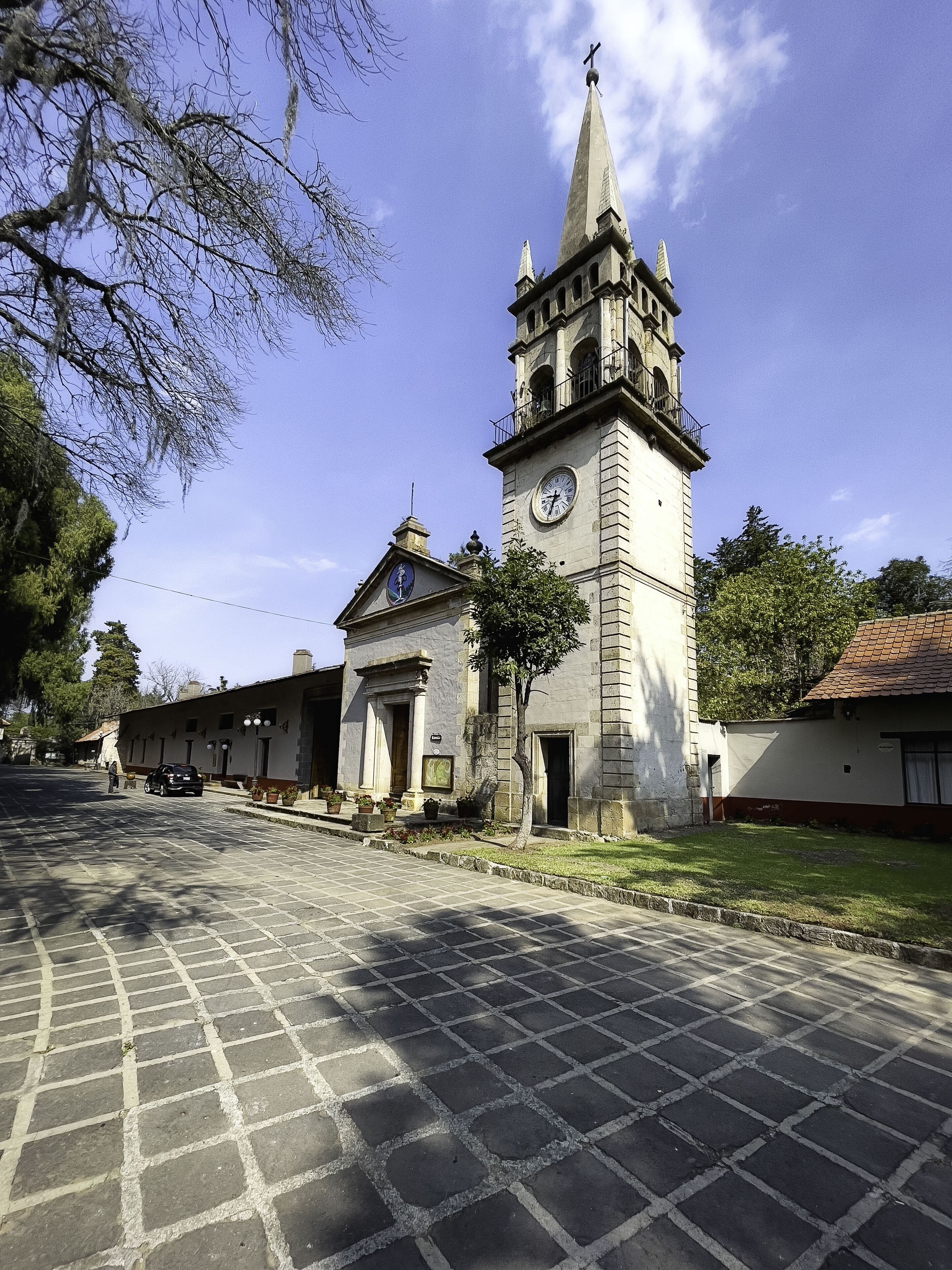 A historic building with a clock tower, paved courtyard, and surrounding greenery.