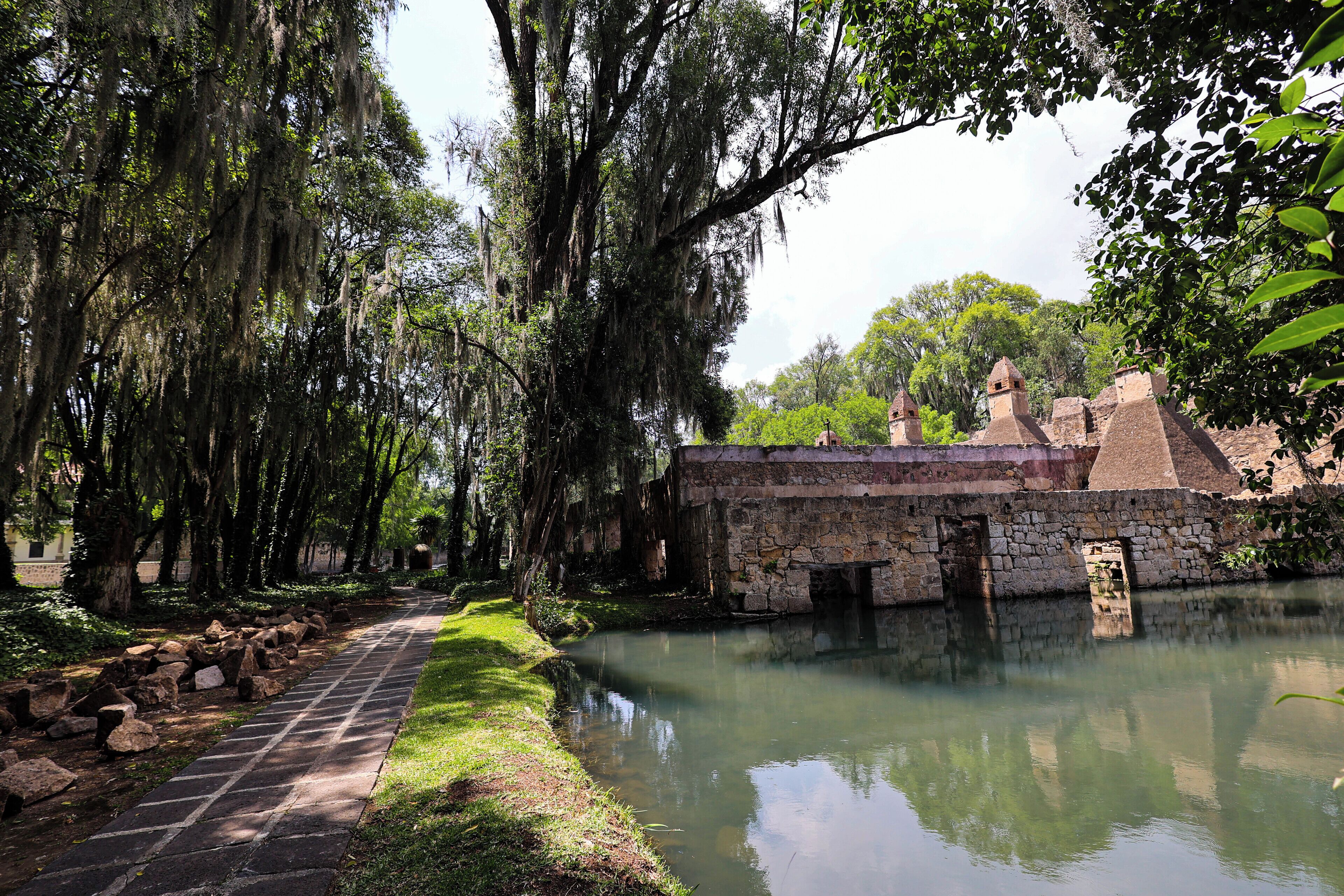 A stone building with a brick roof and a small pond in front.