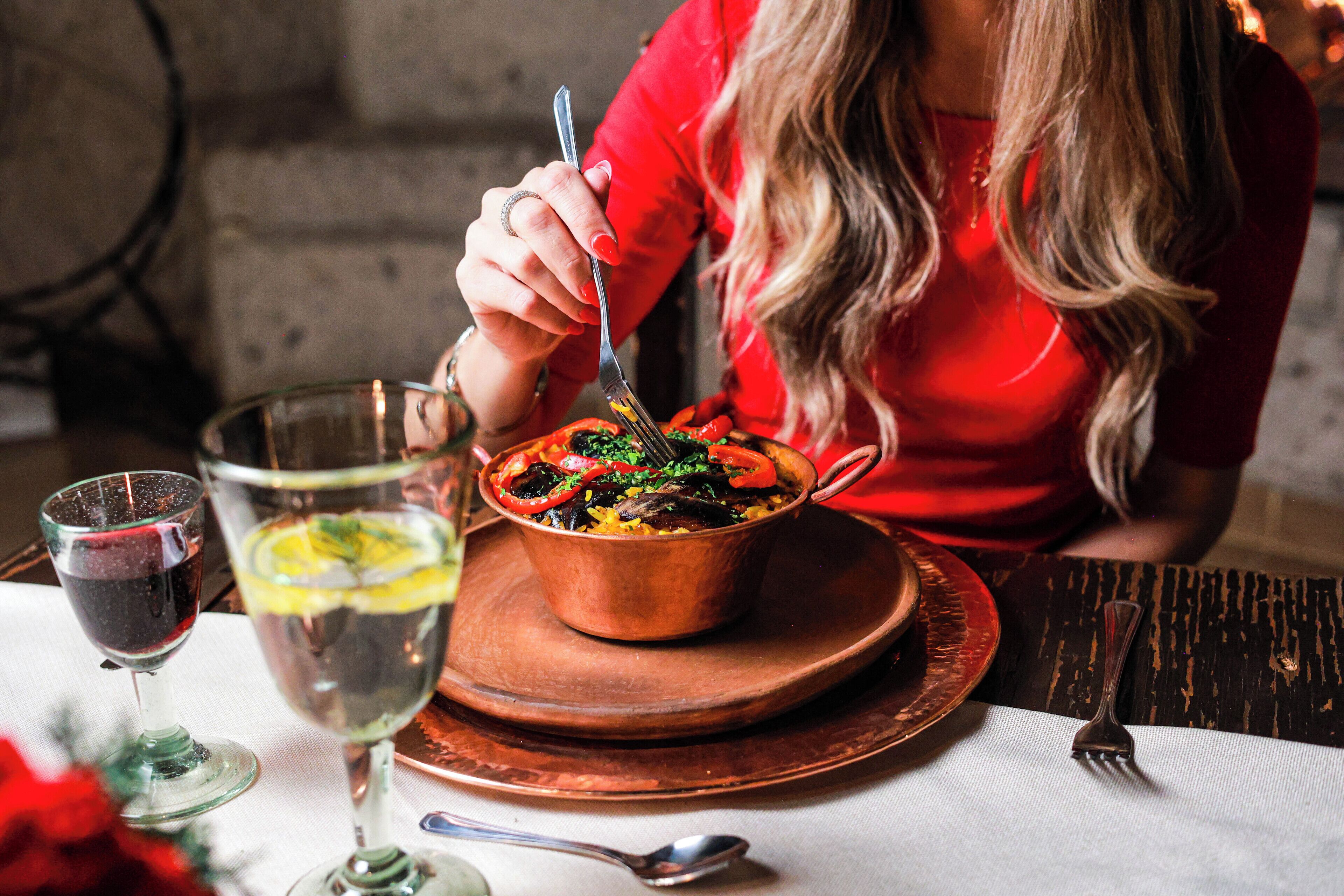 A dining table with a copper pot of food, a glass of red wine, and a glass of water.