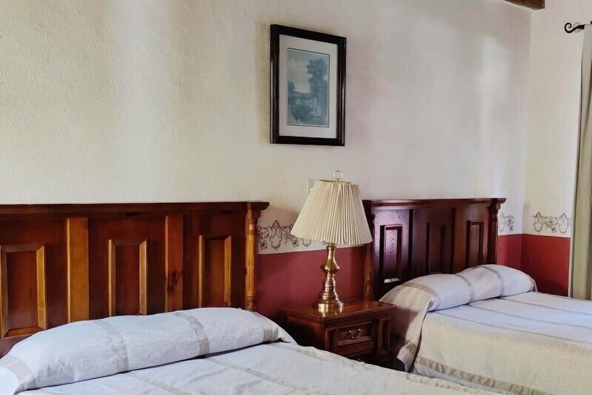 Ein Hotelzimmer mit zwei Betten, einem Holz-Kopfteil, einem Nachttisch mit Lampe und einem gerahmten Bild an der Wand.