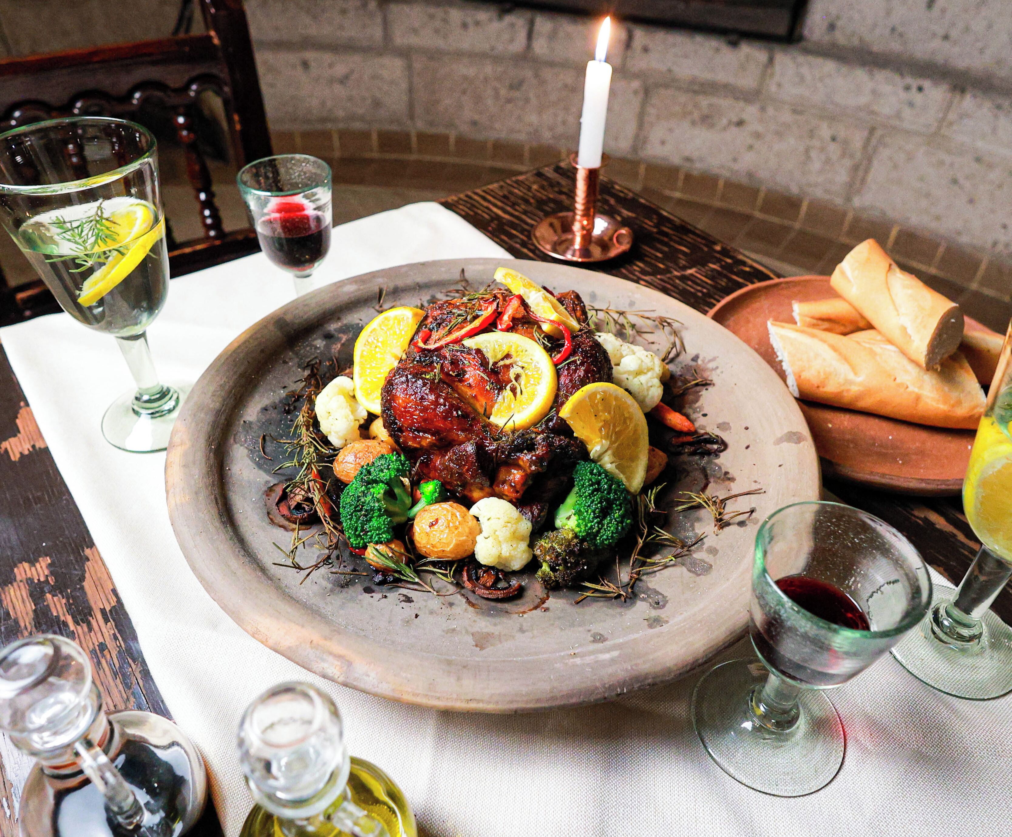 A plate of roasted meat with vegetables, a candle, and glasses of wine on a table.