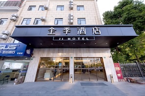 L’entrée d’un hôtel, avec une façade moderne, de grandes portes vitrées et une enseigne en chinois et en anglais.