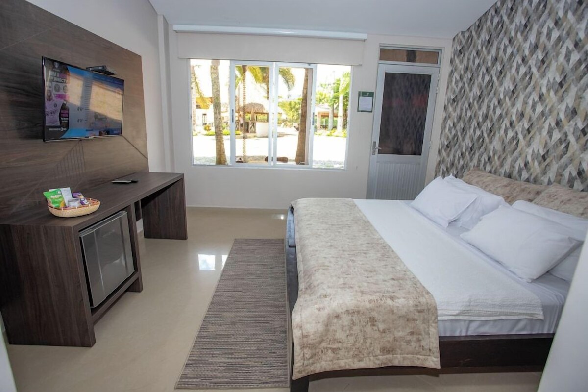 Een moderne hotelkamer met een bed, een bureau met een televisie, een raam met uitzicht op palmbomen en een kamer met een patroon op de muur.