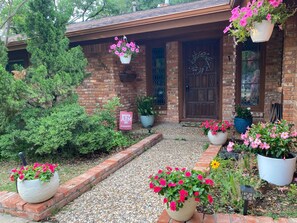 A brick house with a front porch, potted plants, and a gravel pathway.