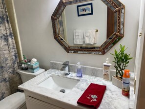 A bathroom with a marble sink, a gold-framed mirror, a toilet, a towel rack with white towels, a red towel, and toiletries on the counter. - Serene House with Charm on Golfcourse! (Bryan)
