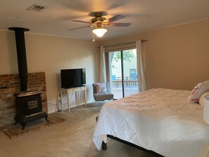 A bedroom with a bed, a TV on a stand, a fireplace, and a balcony with a chair. - Serene House with Charm on Golfcourse! (Bryan)