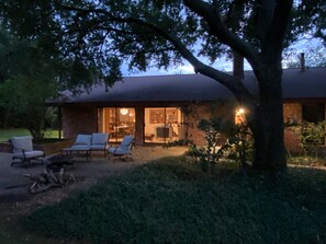 A house with a covered patio area, a large tree, and a well-lit interior visible through the windows. - Serene House with Charm on Golfcourse! (Bryan)
