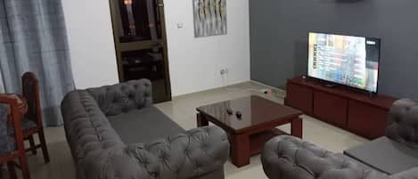 Una sala de estar con un sofá gris, una mesa de centro, un televisor sobre un mueble bajo y una puerta con panel de vidrio.
