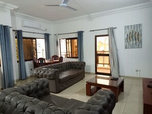 A living room with a sofa, a coffee table, and a dining area with chairs and a table. - 5 min walk from fidjrossè beach, ideal apartment for families (Cotonou)
