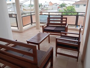 A balcony with wooden furniture, including a sofa and a table, and a view of surrounding buildings. - 5 min walk from fidjrossè beach, ideal apartment for families (Cotonou)