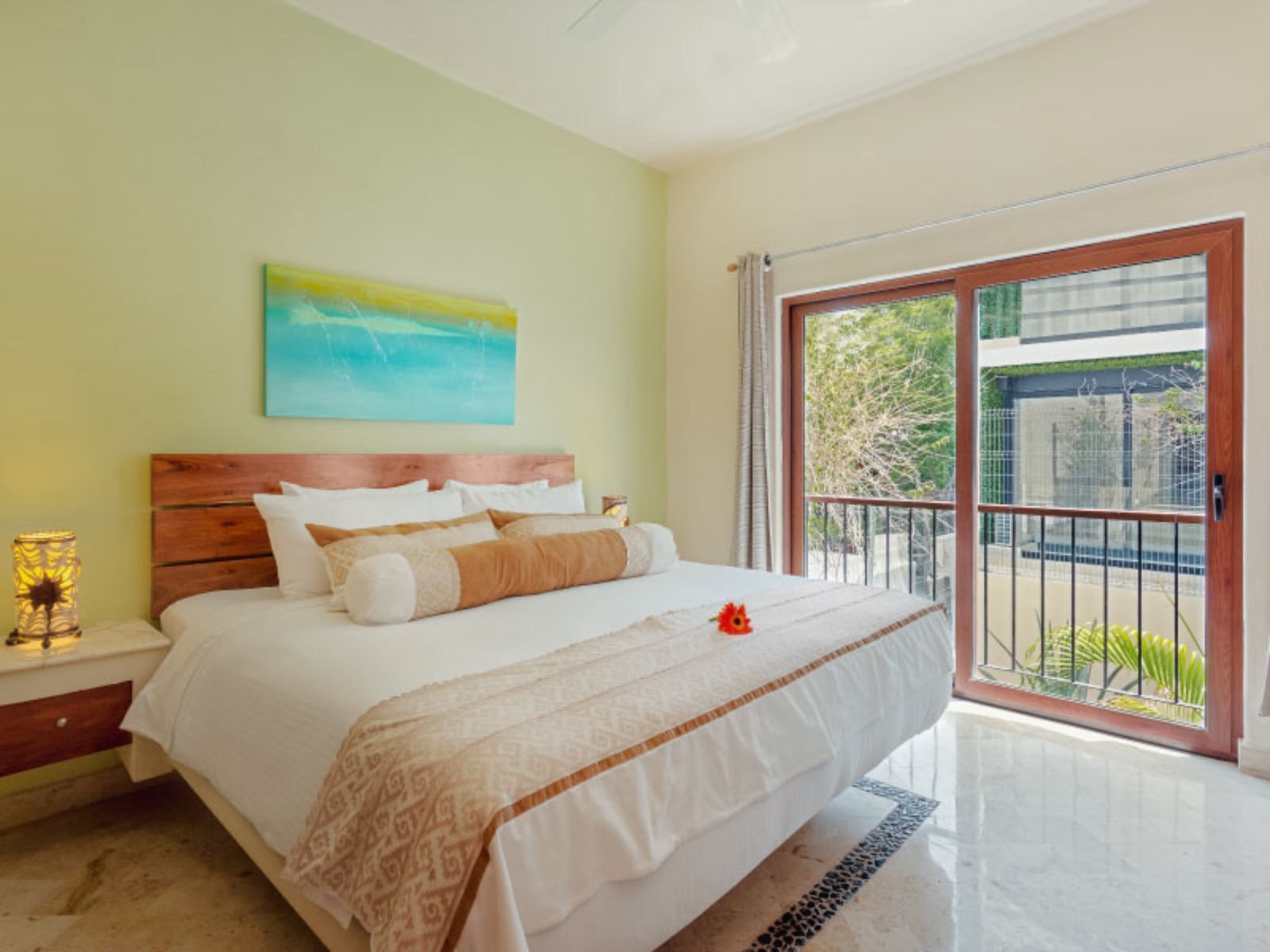 Una camera da letto con un letto grande, un comodino con una lampada, un quadro al muro e un balcone con vista sul verde.