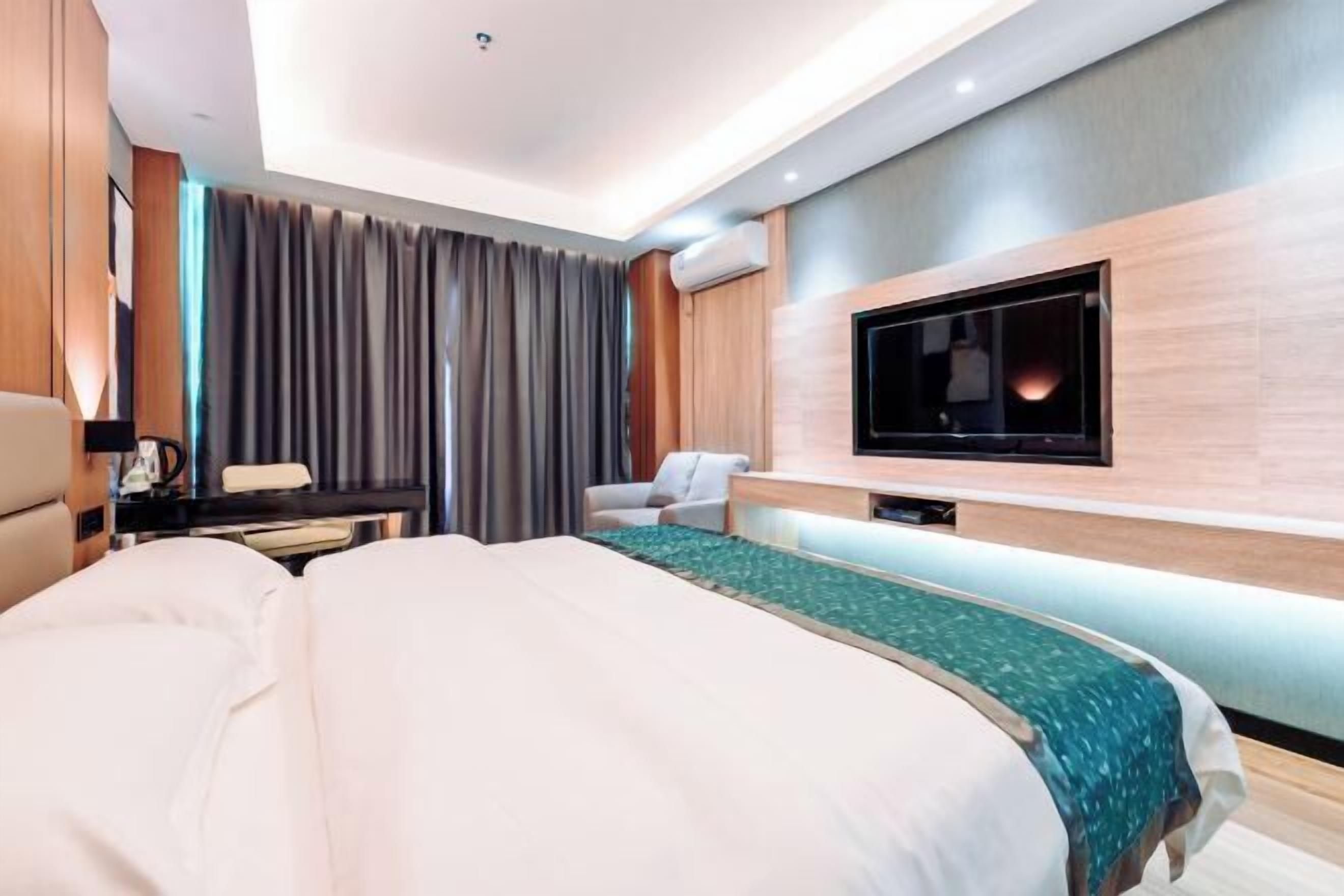 A modern hotel room with a large bed, a desk, a chair, and a flat-screen TV mounted on the wall.