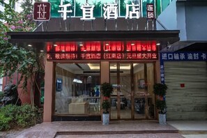 A hotel entrance with a glass facade, signage, and potted plants. - Qianyi Hotel (Yulin Jiangnan Branch) (Yulin)
