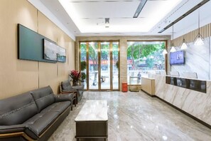 A hotel lobby with a reception desk, a sofa, a coffee table, and a large window with a view of the outdoors. - Qianyi Hotel (Yulin Jiangnan Branch) (Yulin)