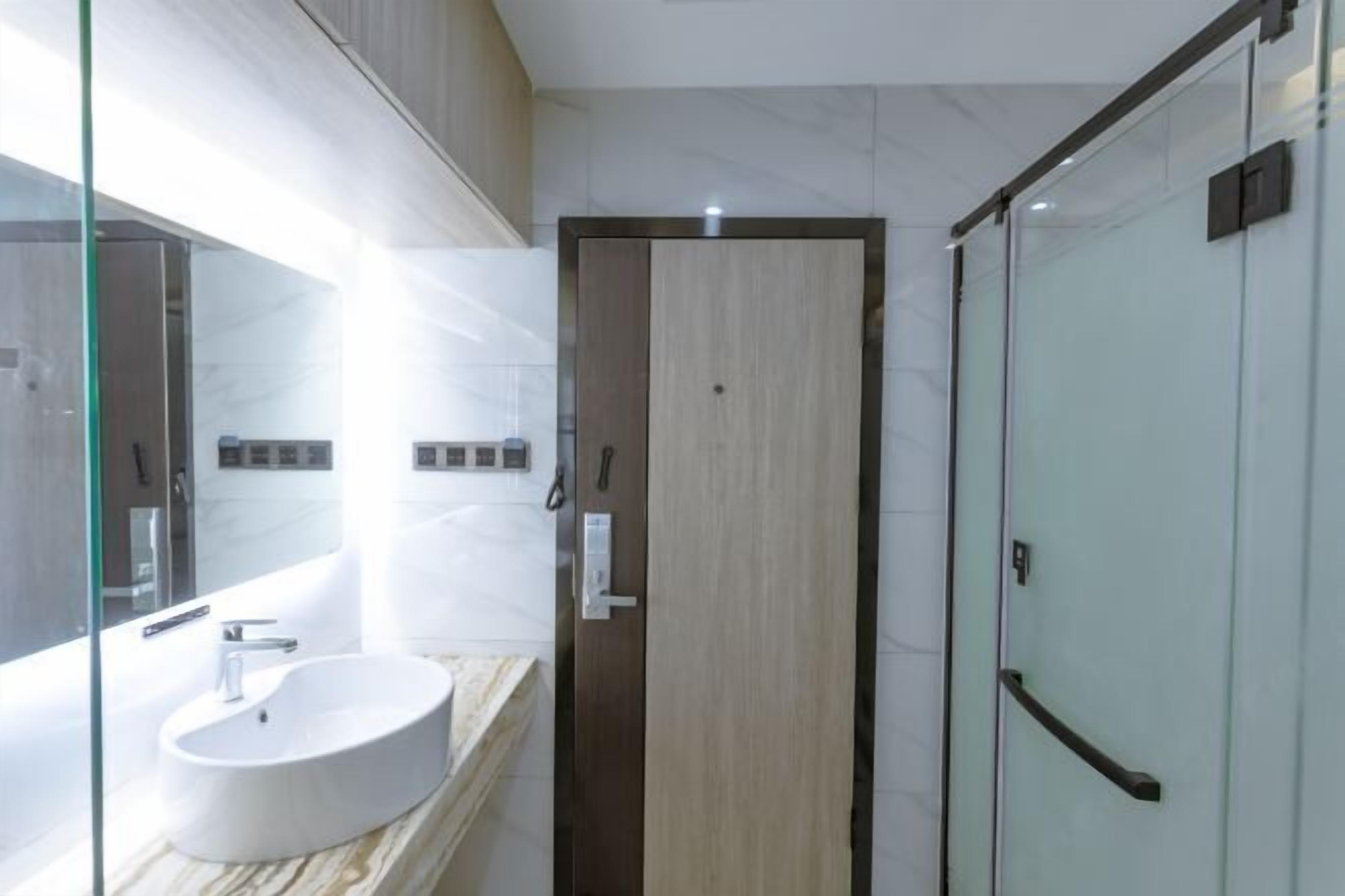 A modern bathroom with a large mirror, a round sink, and a glass shower enclosure.