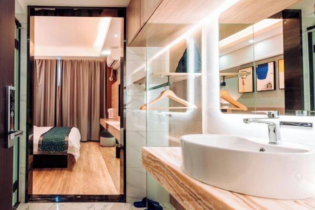 Habitación de hotel moderna con una cama grande, un baño con lavabo y espejo blancos, y vista al interior de la habitación.