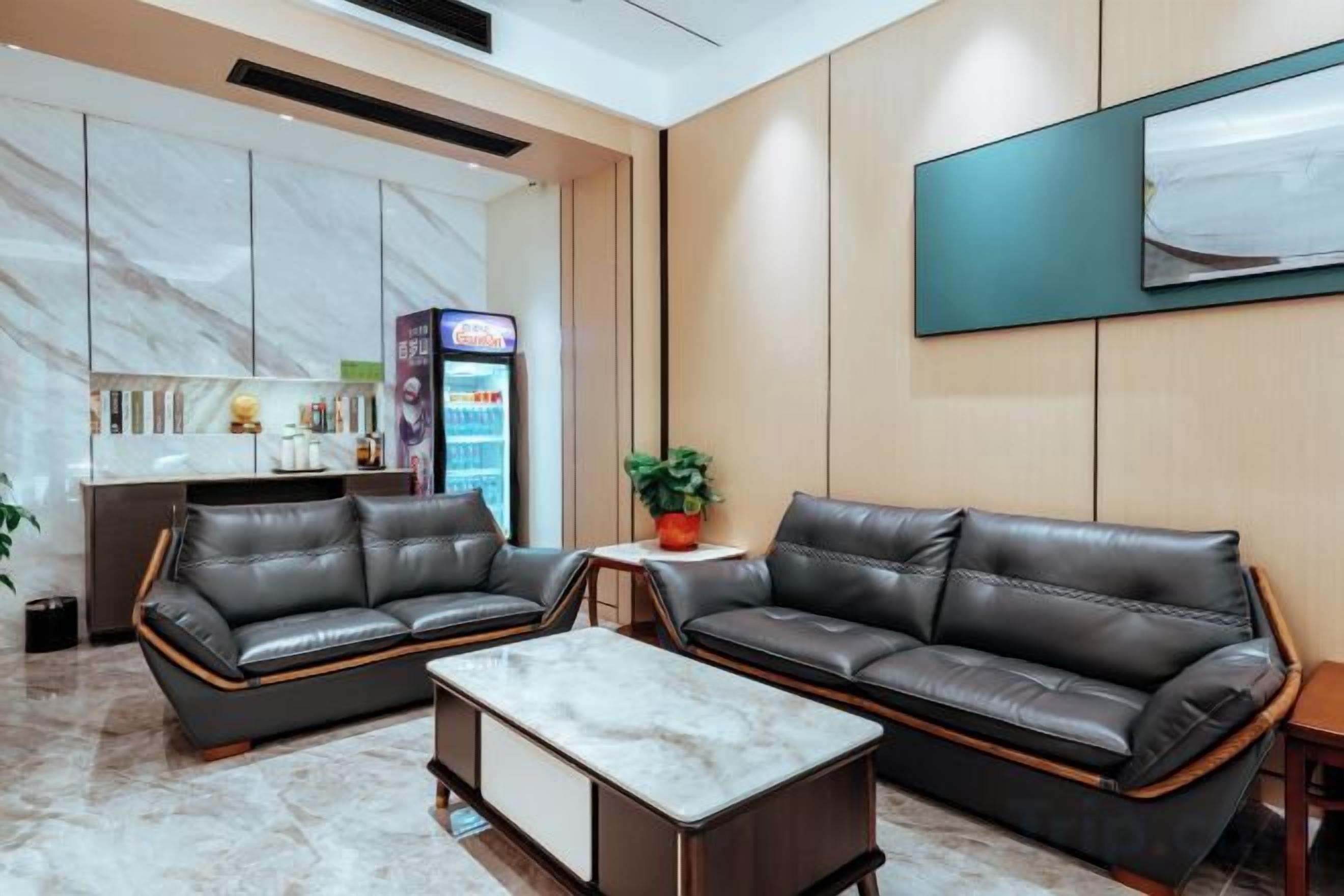 A hotel lobby with leather sofas, a marble coffee table, a small table with a plant, a minibar, and a neon sign.