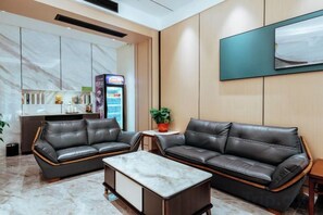 A hotel lobby with leather sofas, a marble coffee table, a small table with a plant, a minibar, and a neon sign. - Qianyi Hotel (Yulin Jiangnan Branch) (Yulin)