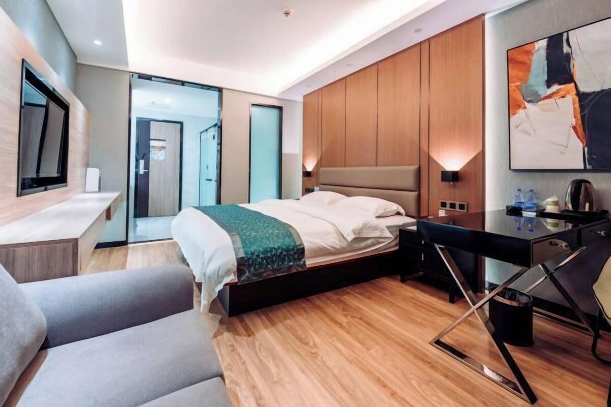 A modern hotel room with a bed, desk, chair, and a TV mounted on the wall.