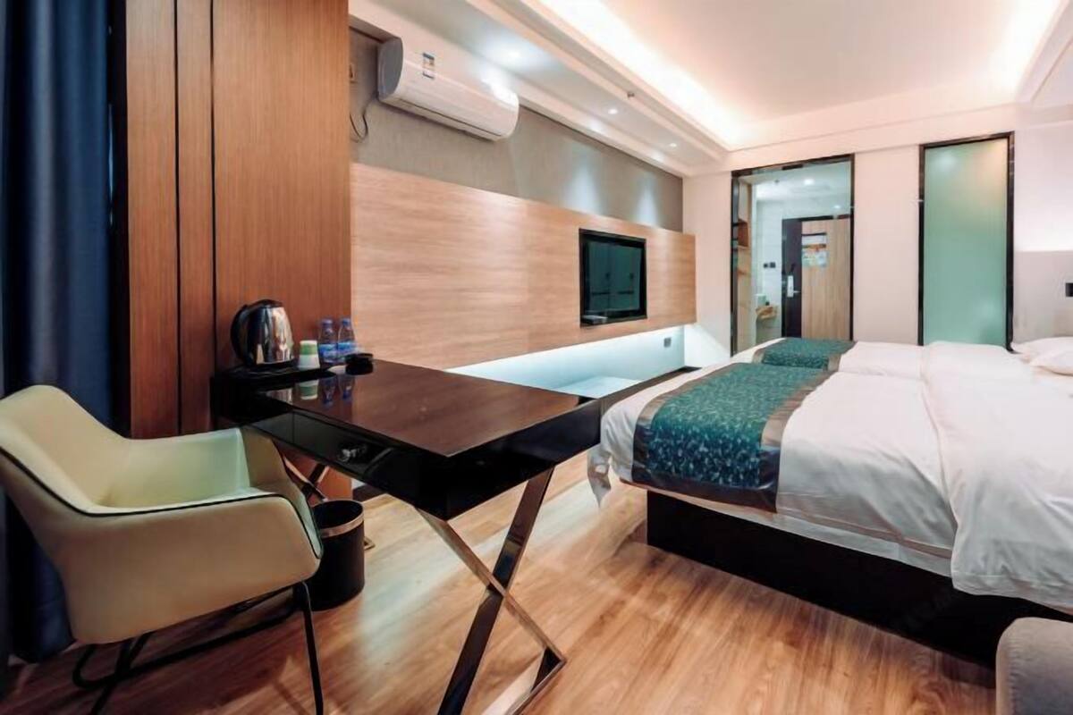 A modern hotel room with a bed, a desk, a chair, a TV, and a minibar.