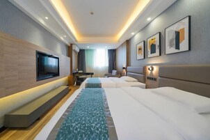 Una habitación de hotel con dos camas, un televisor montado en la pared, un escritorio y una ventana con cortinas.