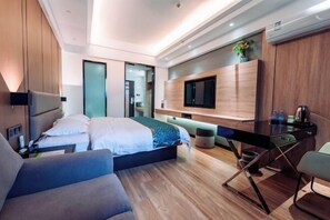 Ein modernes Hotelzimmer mit Bett, Schreibtisch, Fernseher und Pflanze.