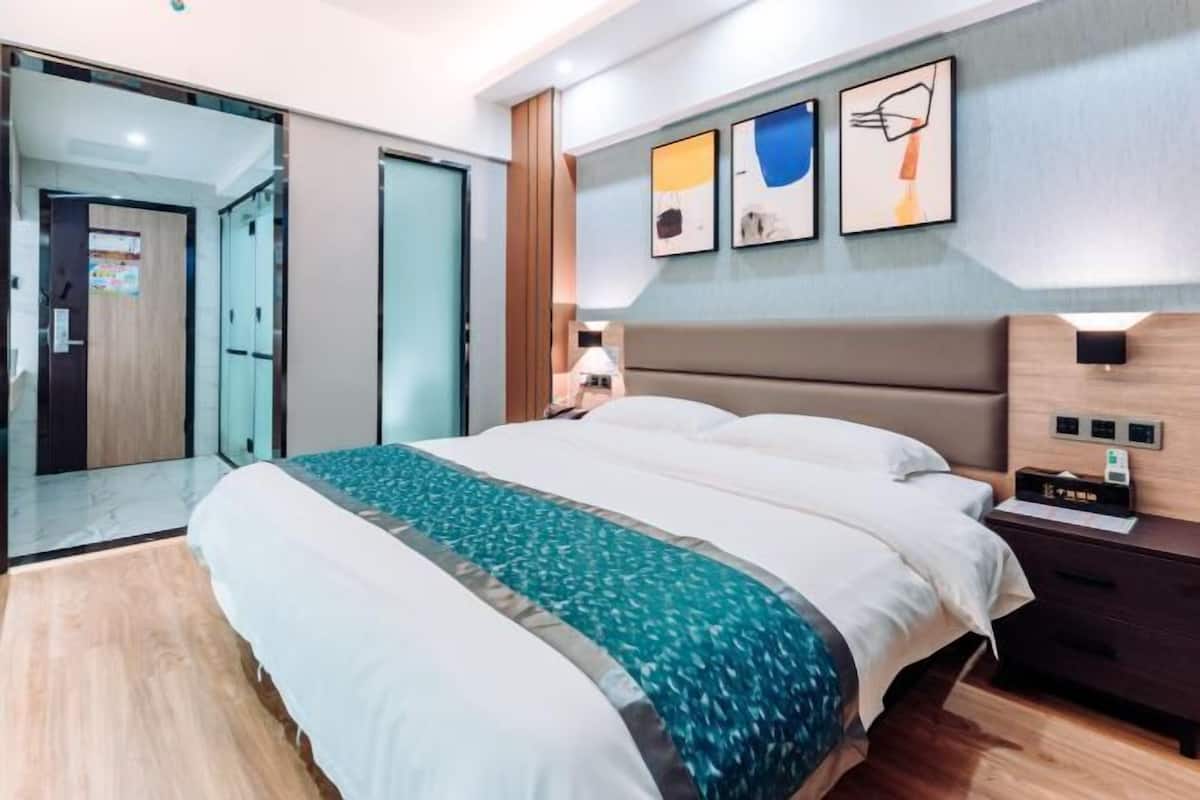 A modern hotel room with a large bed, a nightstand, a wall-mounted lamp, and a door leading to a bathroom.
