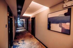 Un pasillo de hotel con puertas a ambos lados, un cuadro en la pared y una lámpara en el techo.