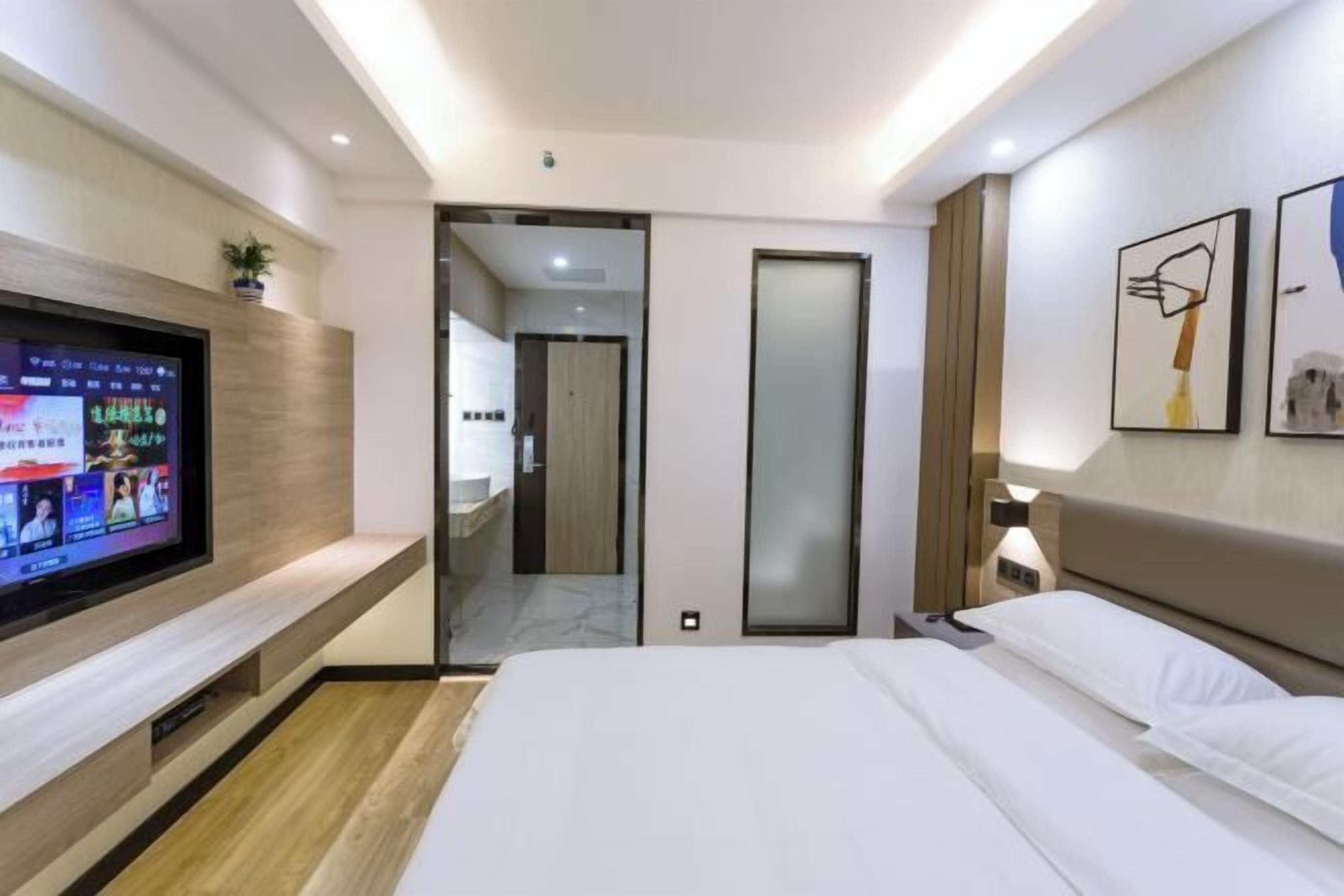 A modern hotel room with a bed, a TV, a wall-mounted plant, and a door leading to a bathroom.