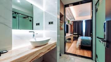 A modern bathroom with a marble vanity, a large mirror, and a view into a bedroom with a bed and a small table.