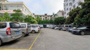 Un parking où sont garées plusieurs voitures et fourgonnettes, entouré d’immeubles et d’arbres.