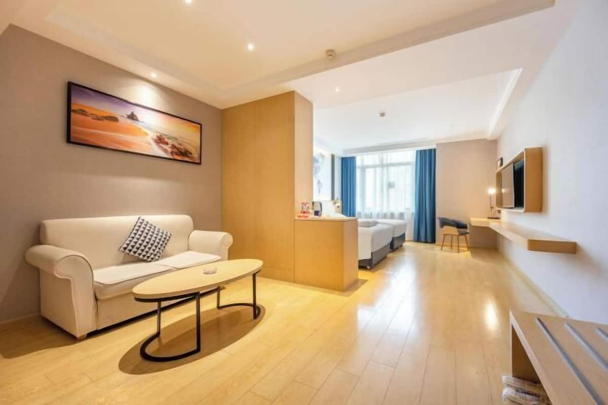 Una camera d'albergo moderna con un divano, un tavolino, una scrivania, una TV e un quadro appeso al muro.