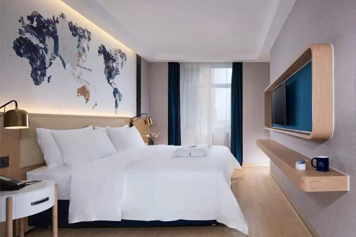 Una camera d'albergo moderna con un letto grande, una TV a schermo piatto montata a parete, un comodino e un'opera d'arte raffigurante una mappa del mondo.