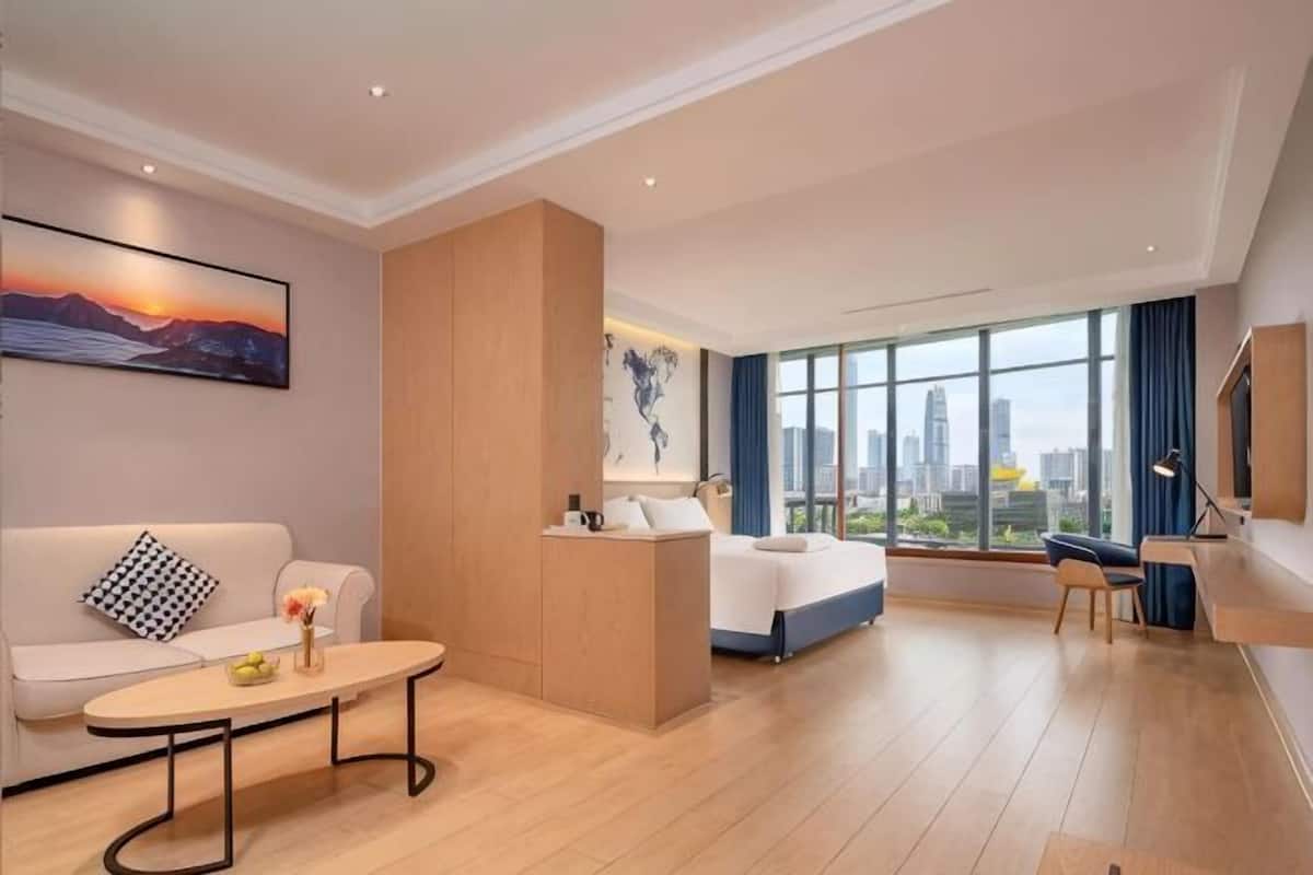 Una camera d'albergo con un letto, un divano, una scrivania e un'ampia finestra con vista sulla città.