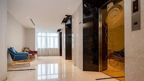 En modern hotellobby med ett marmorgolv, en blå fåtölj, en röd fåtölj och en glashiss.