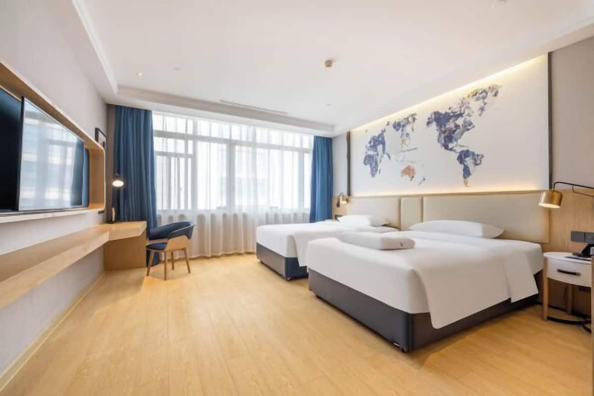 Camera d'hotel con due letti, una scrivania, una sedia, una mappa del mondo appesa al muro e una finestra con tende.